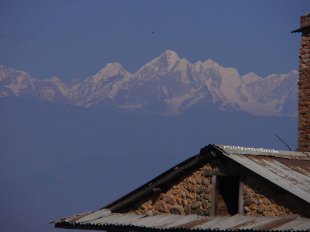 An attic window in the foreground. Snow caped mountains in the background. A blue sky