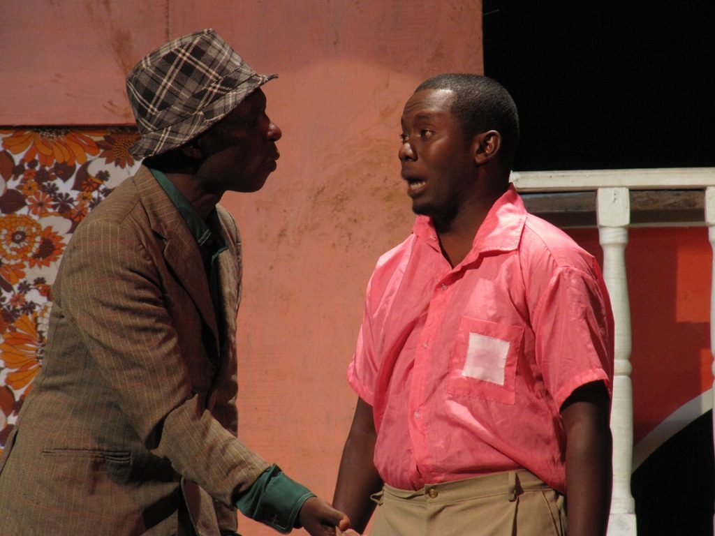 Two male actors on a theater stage, staring at each other