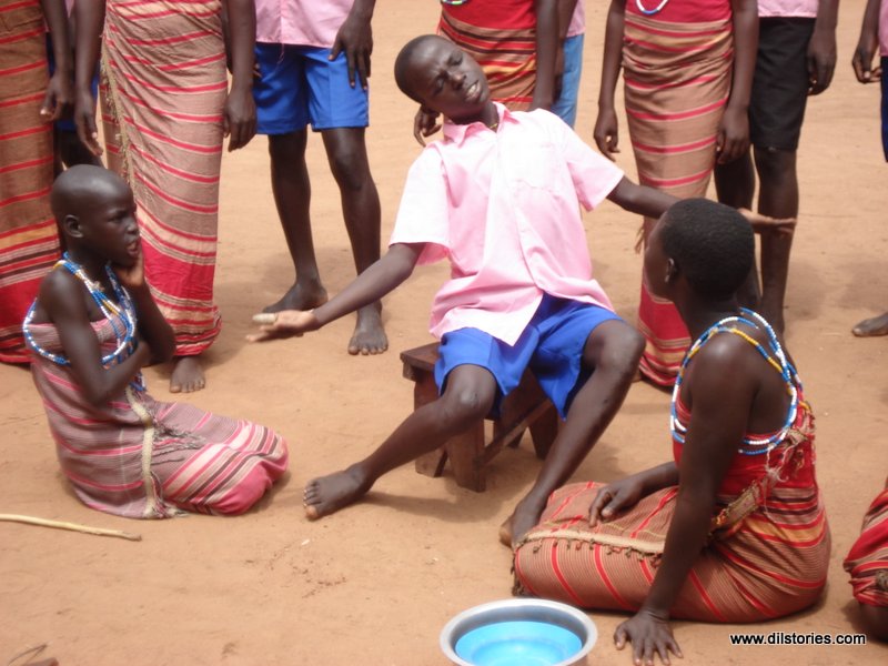 Child actors in costume. One boy sits on a stool, two girls sit on the ground.