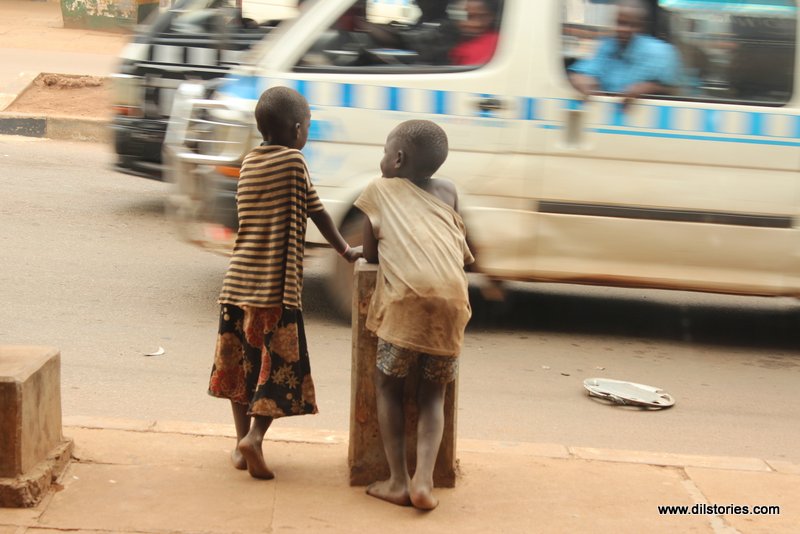 Two children with their backs to camera, a commuter taxi in the background, a city street