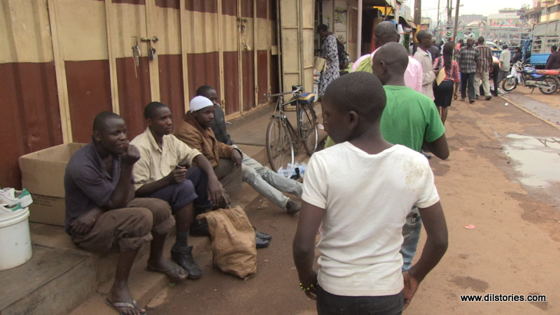 A line of street children walk past men seated on the streets in downtown Kampala