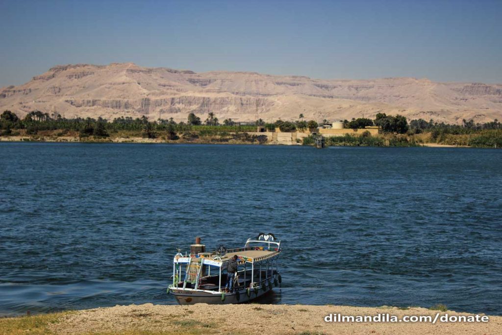 A boat anchored in the banks, the river Nile in the midground, and desert mountains of the West Bank Luxor in the background