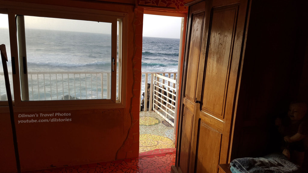A window and and open door. A balcony. The sea in the background. Daytime