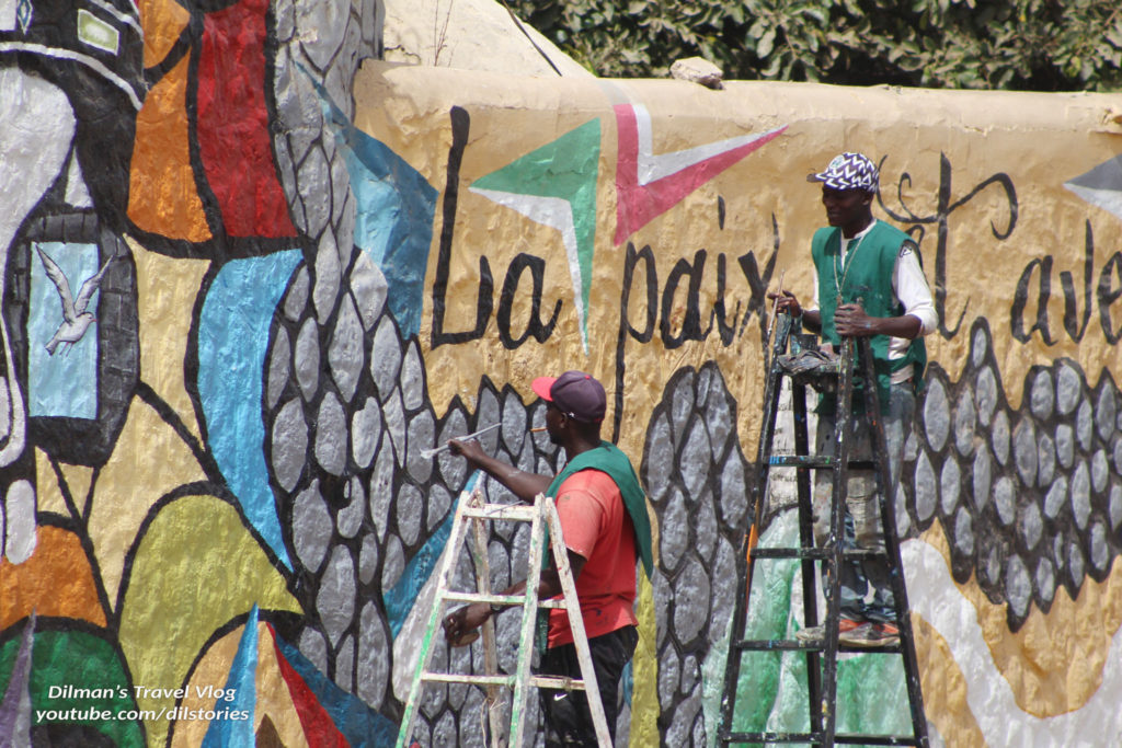 Two artists on ladders, male, painting a mural, which has a multitude of colors