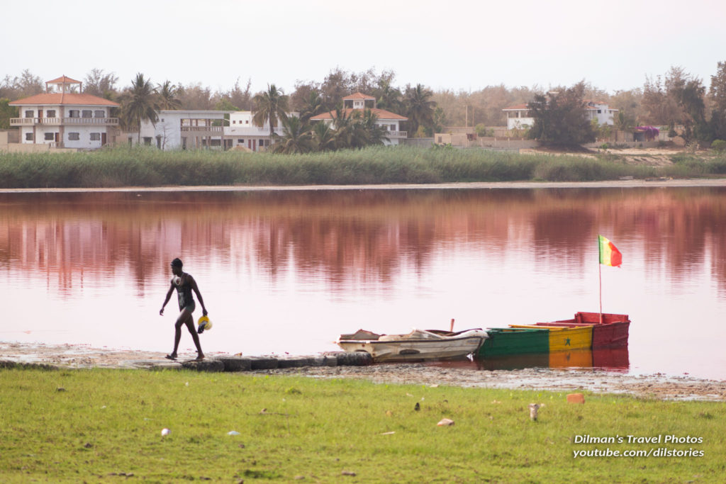 A man walking away from a boat with pinkish waters of Lac Rose in Senegal