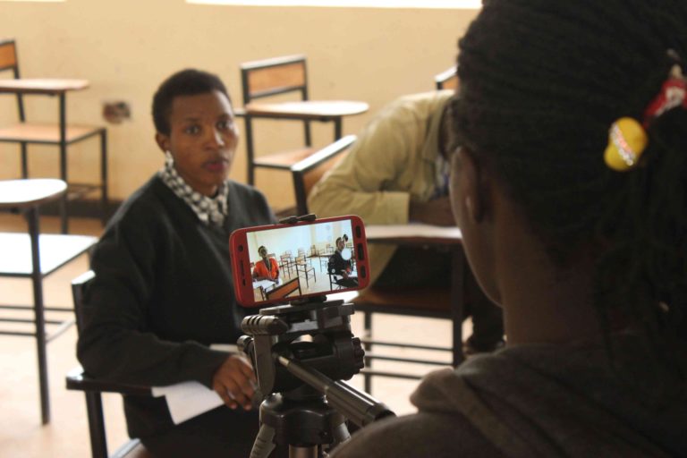 Film training session. A woman with her back to the camera using a smart phone, Samsung S7, set on a tripod, to film an actress