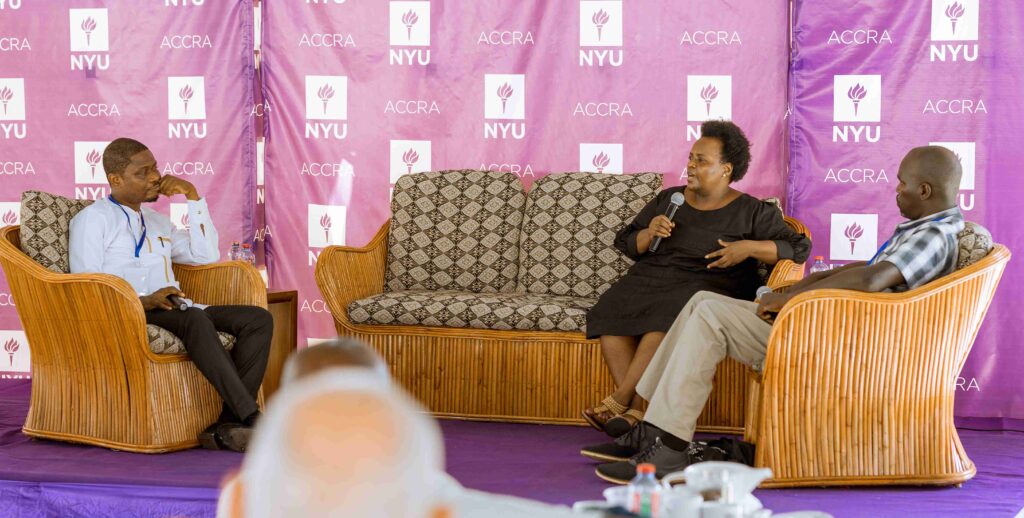Three people on a stage, two male, one female, discussing. The lady is in black and holds a microphone. A purple backdrop has NYU Accra.