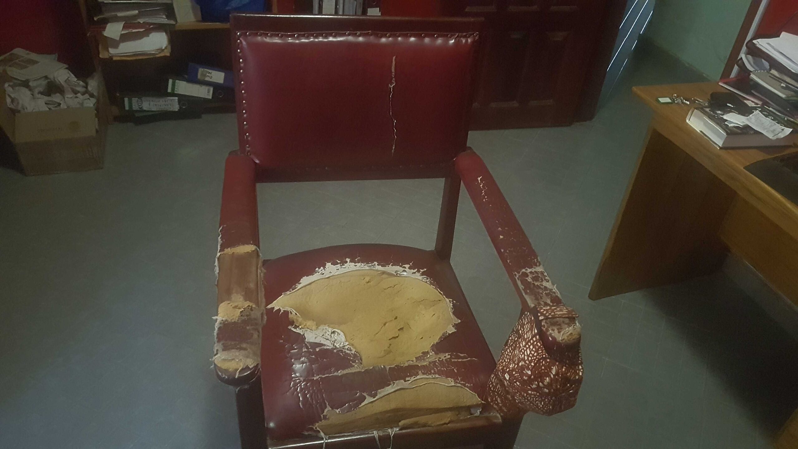 An old wooden arm chair covered with red leather. The leather is torn up and the sponge shows in some places.