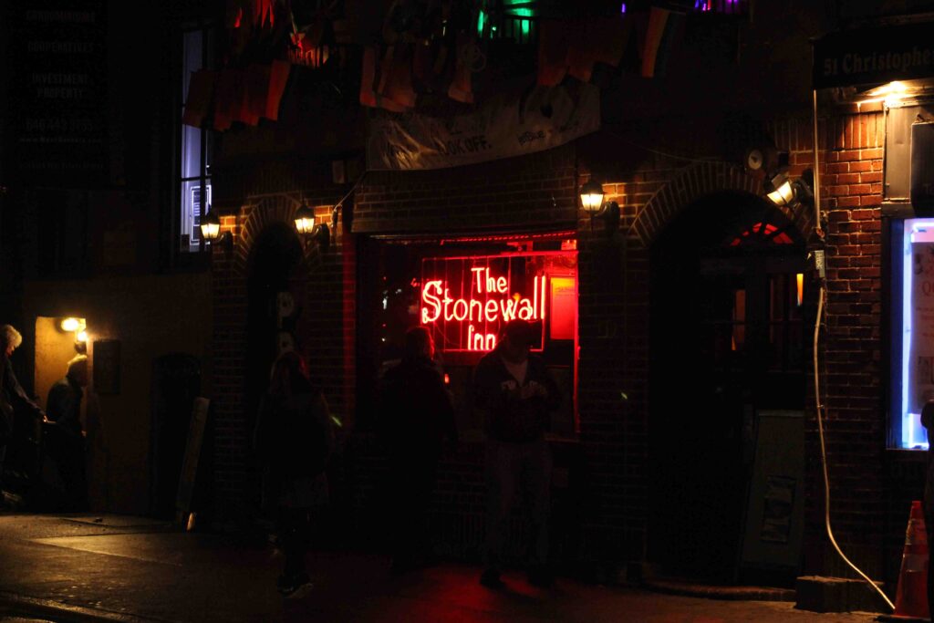 The street side of a bar, with the name written in neon lights.
