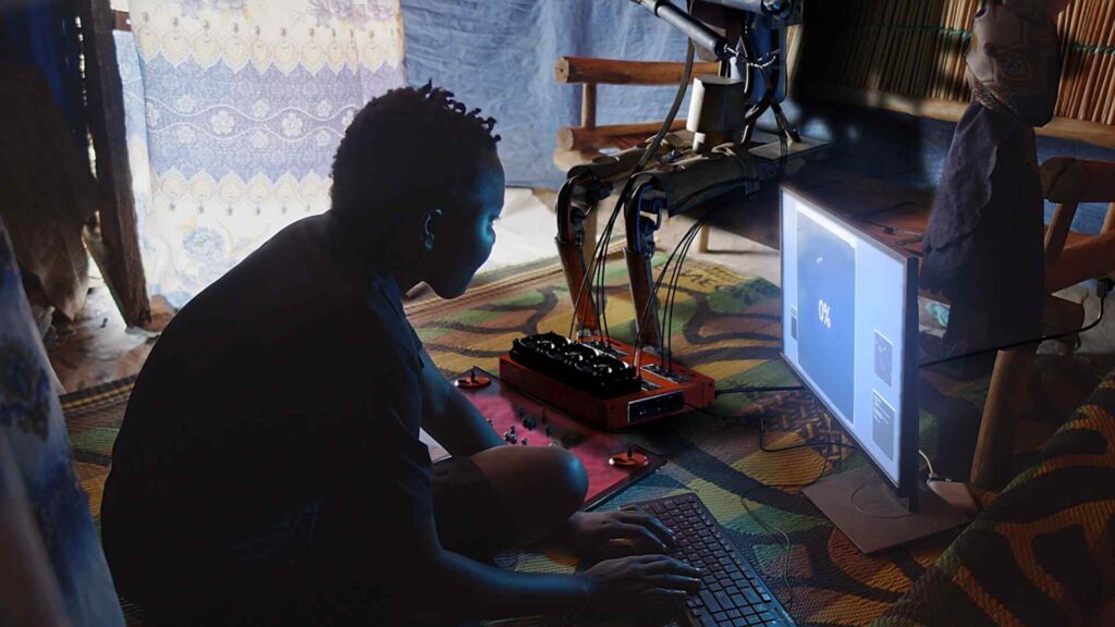 A young African woman works a low-tech but futuristic computer, using it to repair a robot, which is in the background.